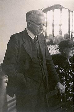 Sir Walter Murdoch standing behind a chair