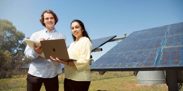 a male and a female student looking at a laptop with solar panels in the background