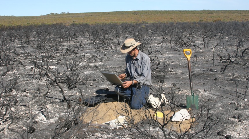 Dr Fontaine kneeling with a laptop in burn area