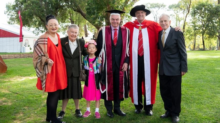 Governor of Western Australia Kim Beazley AC shakes the hand of Murdoch University Vice Chancellor Professor Andrew Deeks, both in full academic regalia, with Professor Deeks' mother, father, wife and daughter.