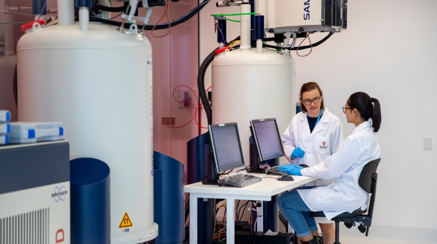 Two female researchers operating at large NMR lab equipment