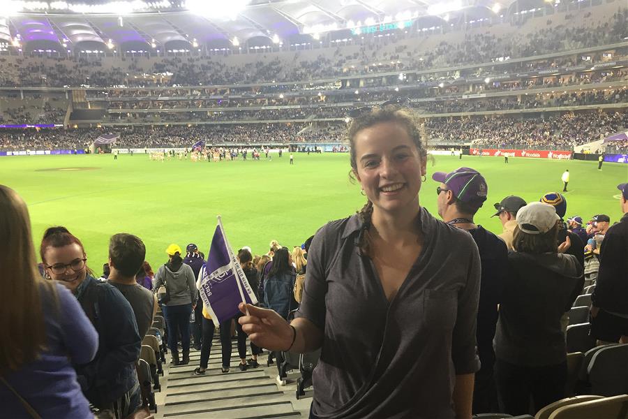 Young woman holding a Fremantle Docker flag smiling, with Optus Stadium in background