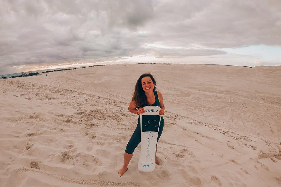Young woman posing with a sandboard in dunes