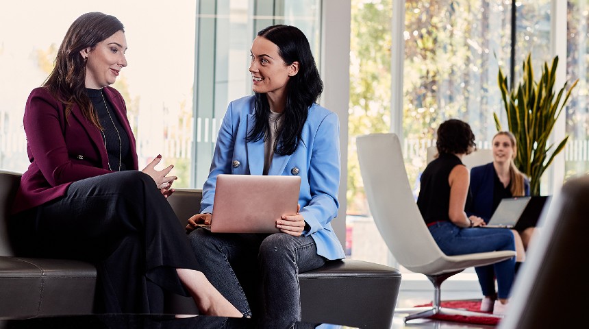Two women sitting on a couch with a laptop having a business meeting