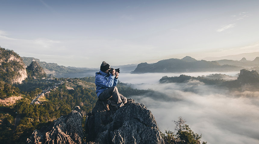 Man taking a photo at the top of a misty mountain range