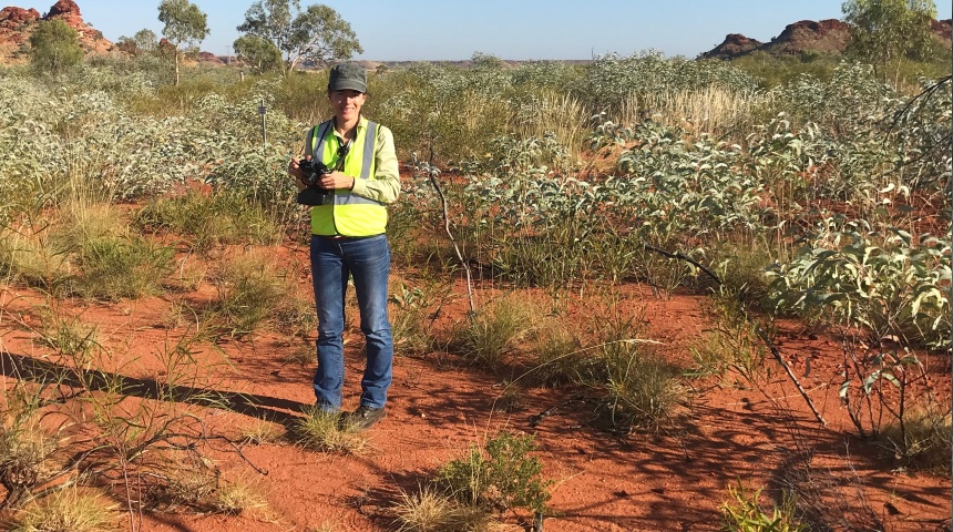 Associate Professor Rachel Standish standing in a red earth field with native shrubs