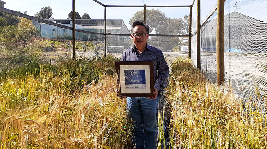 Chengdao Li holding his award near some barley