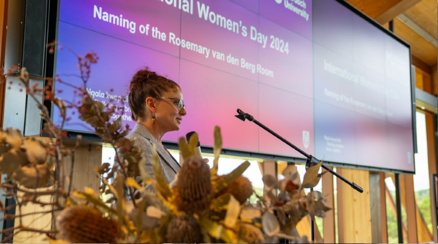 Dr Rebecca Bennett presenting at a lectern on International Womens Day