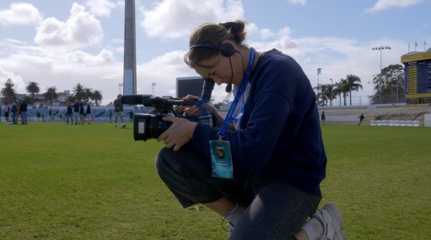Student looks through video camera on a sports field