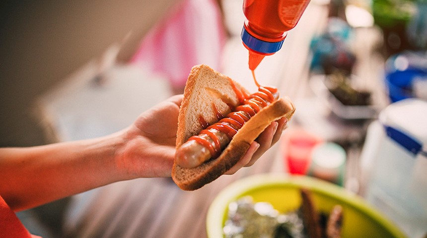 Image of person's hand holding piece of bread with barbecued sausage 