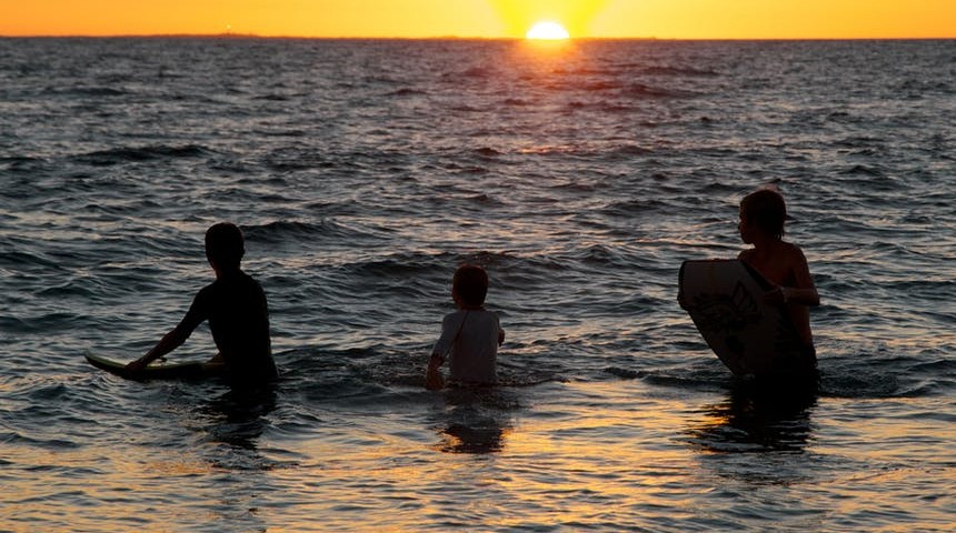 Three young people swimming in the ocean at sunset.