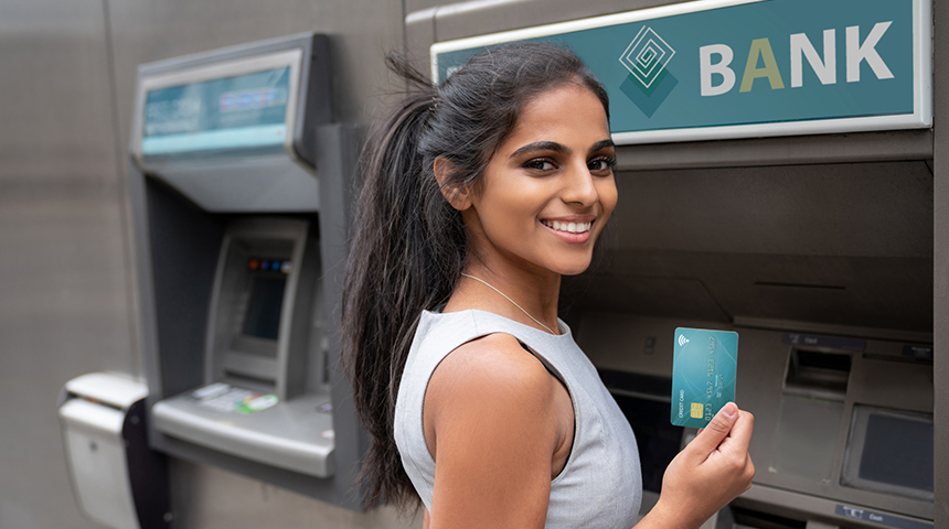Female student smiling in front of ATM holding up a debit card