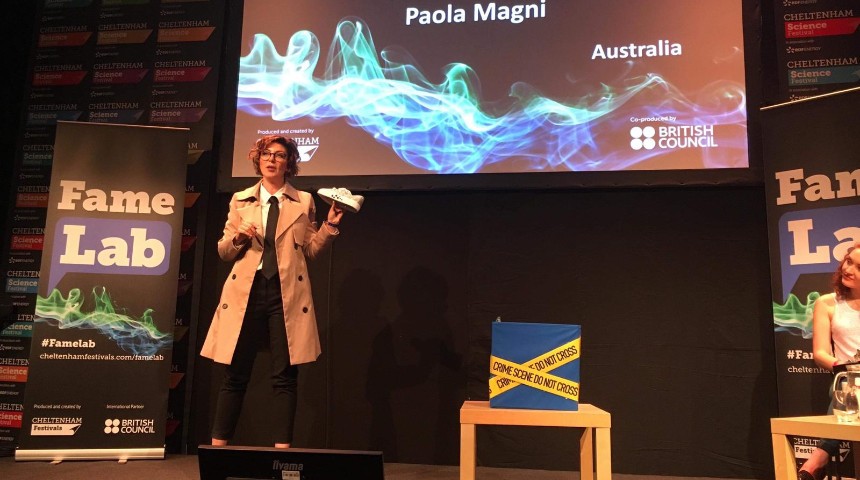 Paola Magni holding a shoe performing at the International FameLab finals 2019