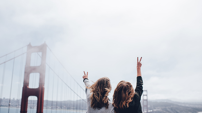 Two girls waving their hand in the air in front of bridge