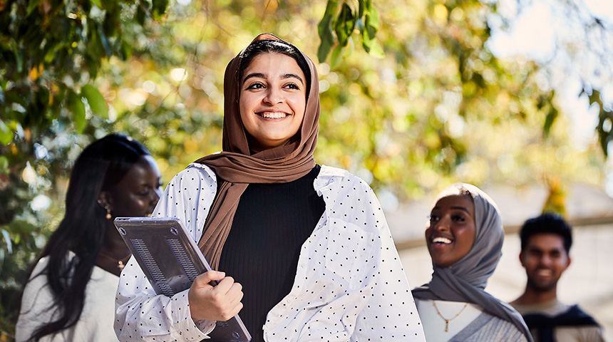Female student wearing hijab smiling and holding laptop.