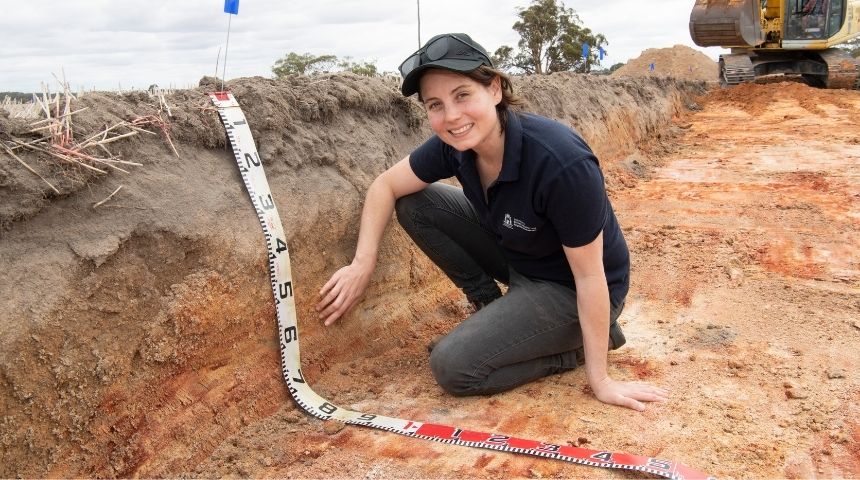 Soil scientist Jenni Clausen kneeling in dirt with a giant measuring tape
