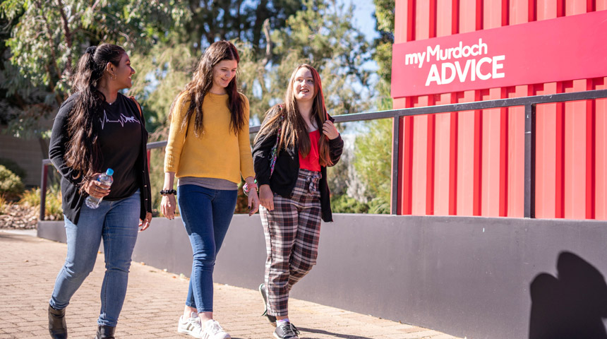 Three students walking near an advice hub
