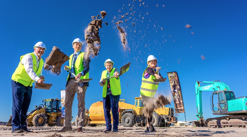 Four people throwing soil from spades at construction site of new food facility