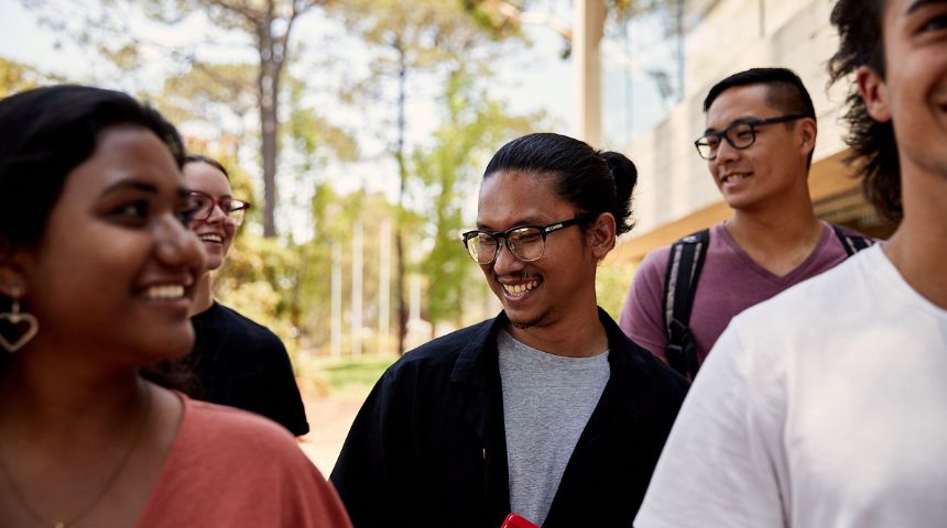 Close up of group of students walking through campus, student in middle is in focus and is smiling off camera