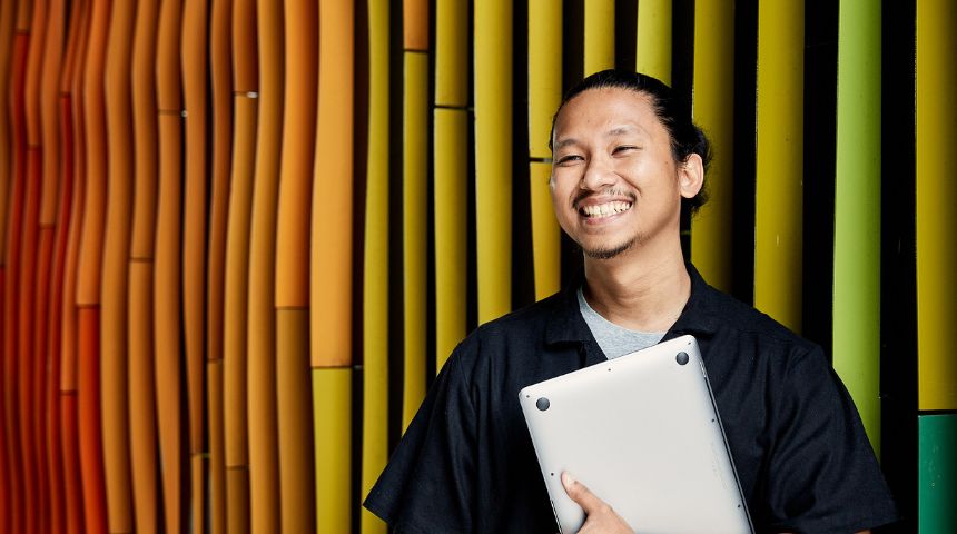 Murdoch student smiling off camera holding a laptop.