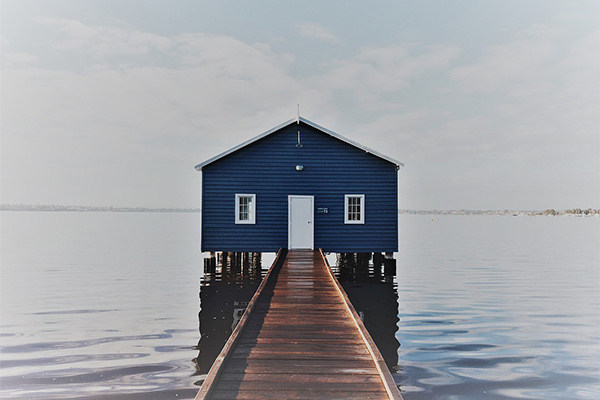 Blue boathouse with jetty surrounded by water and sky