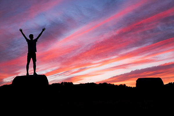 Silhouette of person standing at the top of a mountain with their arms in the air