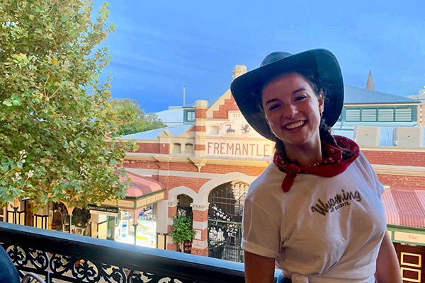 Young woman in cowboy hat and white t-shirt smiling and posing outside of Fremantle Markets