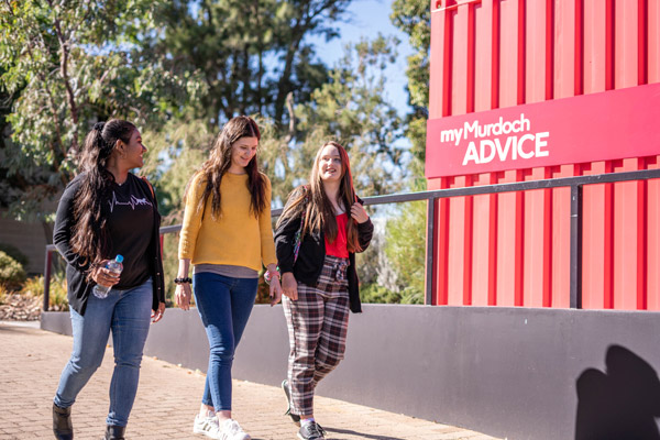 Three students walking near an advice hub