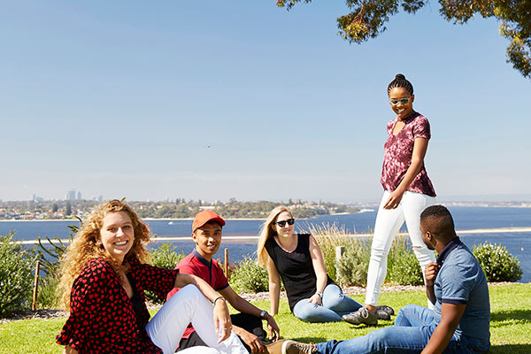 A mix of students smiling and sitting at Kings Park with the Perth CBD in the background